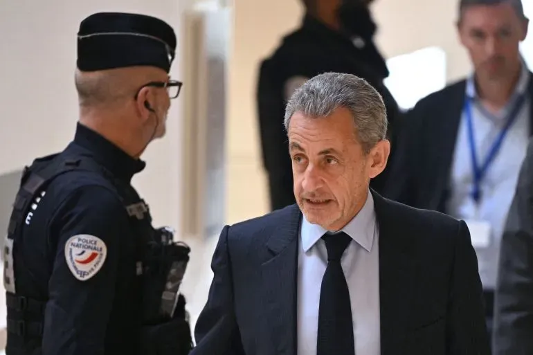 نيكولا ساركوزي، الرئيس الفرنسي السابق، يتحدث أثناء محاكمته، مع وجود ضباط الشرطة في الخلفية، في سياق قضايا الفساد واستغلال النفوذ.