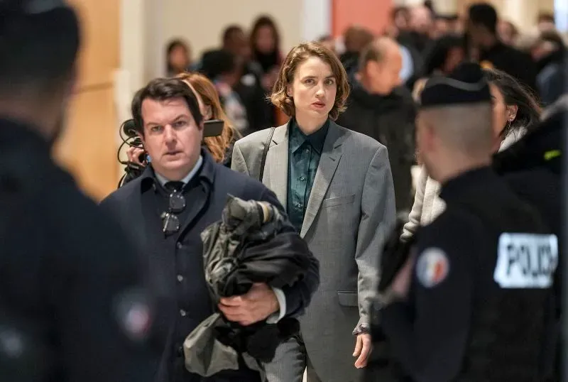 امرأة ترتدي بدلة رسمية تسير في قاعة المحكمة، محاطة بأشخاص آخرين، في سياق محاكمة تتعلق بقضية اعتداء جنسي في السينما الفرنسية.