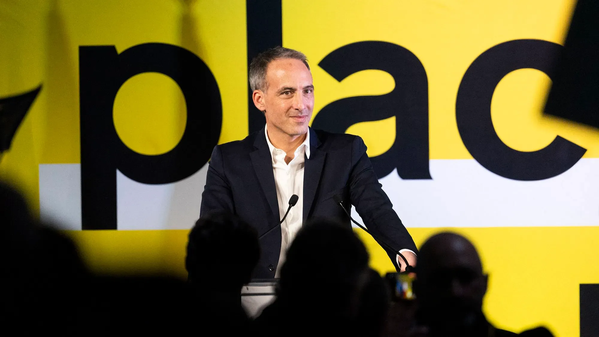 رافائيل غلوكسمان، سياسي فرنسي، يتحدث في تجمع، داعياً لإعادة تمثال الحرية إلى أمريكا، مع خلفية تحمل شعار حزبه "بليس بوبليك".