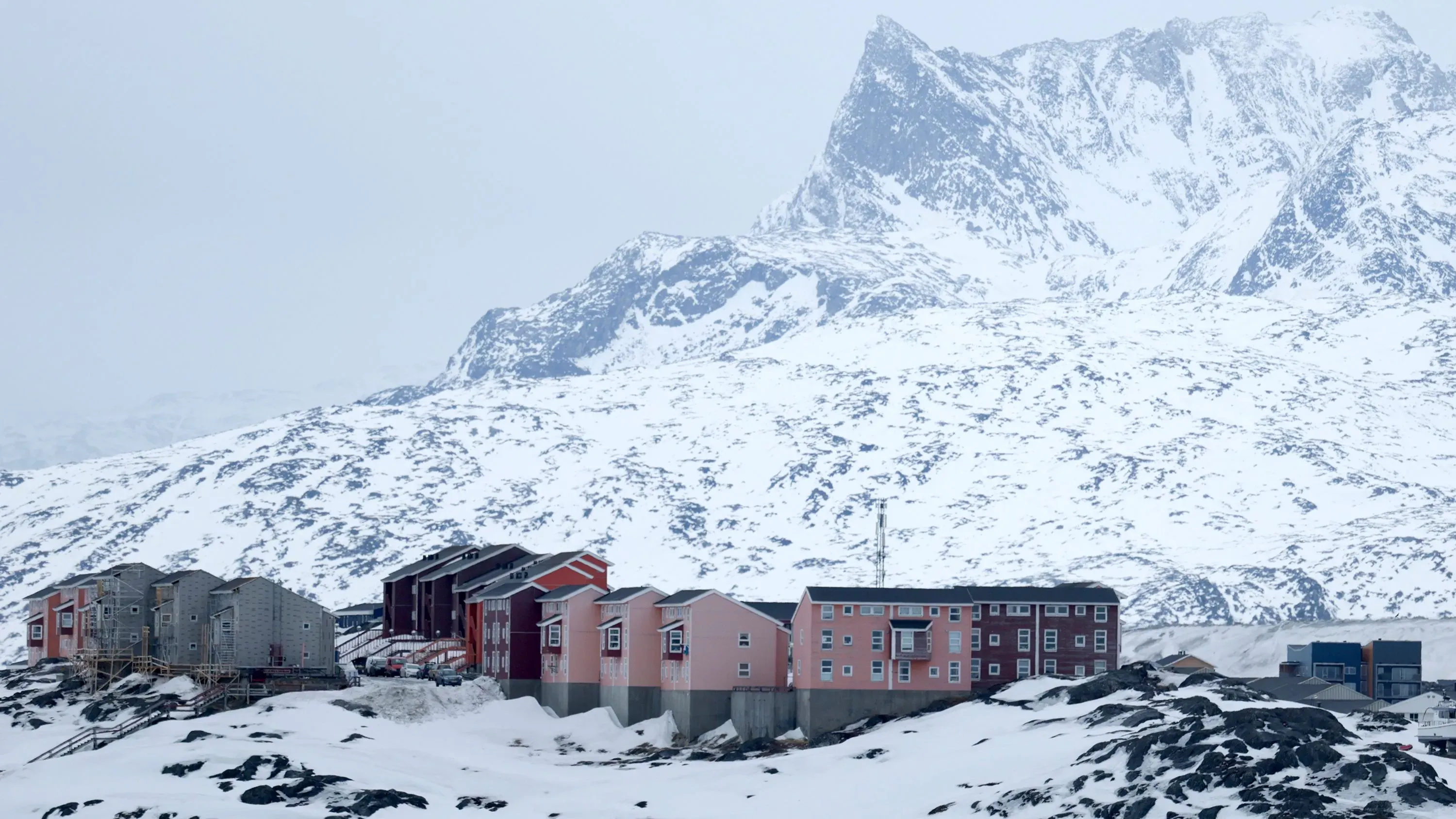 منازل ملونة في غرينلاند محاطة بالثلوج، مع جبال شديدة الانحدار في الخلفية، تعكس جمال وتحديات المنطقة القطبية.
