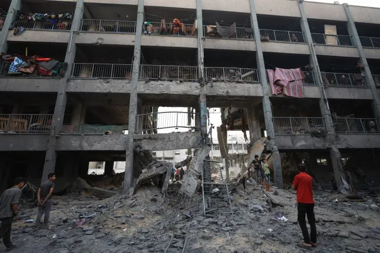 طلاب فلسطينيون يقفون أمام مبنى مدمر في غزة، حيث يستعدون لامتحان الثانوية العامة وسط ظروف صعبة نتيجة النزاع المستمر.