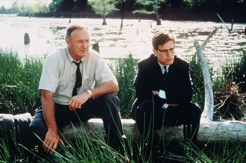 مشهد من فيلم يظهر شخصيتين، إحداهما رجل مسن يرتدي بدلة، يجلس بجانب شاب في بدلة، محاطين بالطبيعة.