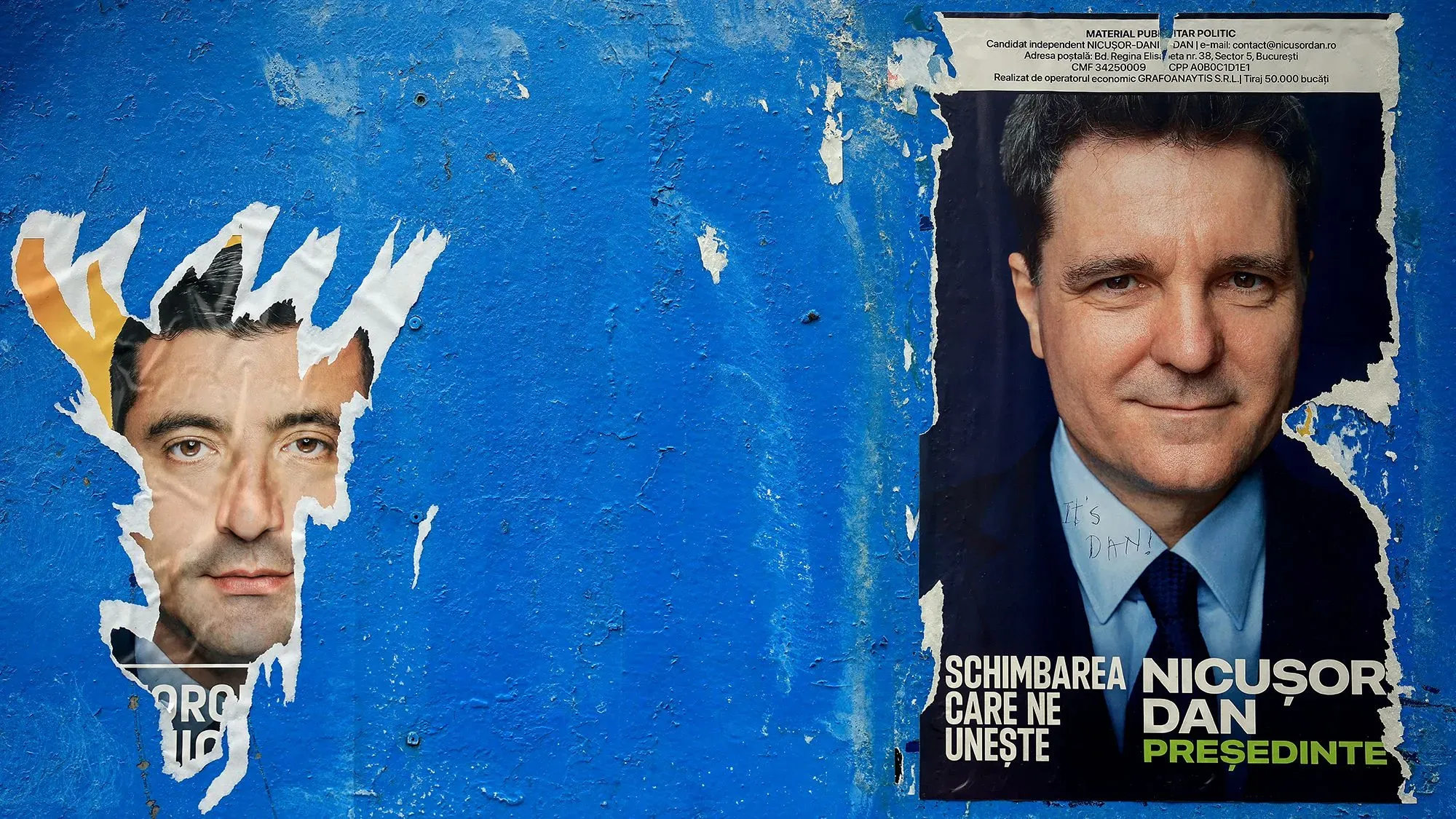 ملصق انتخابي لجورج سيميون ونيكوسور دان على جدار أزرق، يعكس التوترات السياسية في الانتخابات الرئاسية الرومانية.
