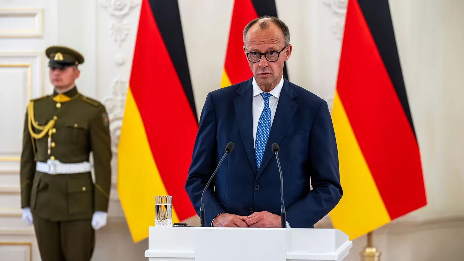 المستشار فريدريش ميرتس يتحدث في مؤتمر صحفي في ليتوانيا، مع العلمين الألماني والليتواني خلفه، مؤكدًا على أهمية الأمن في المنطقة.