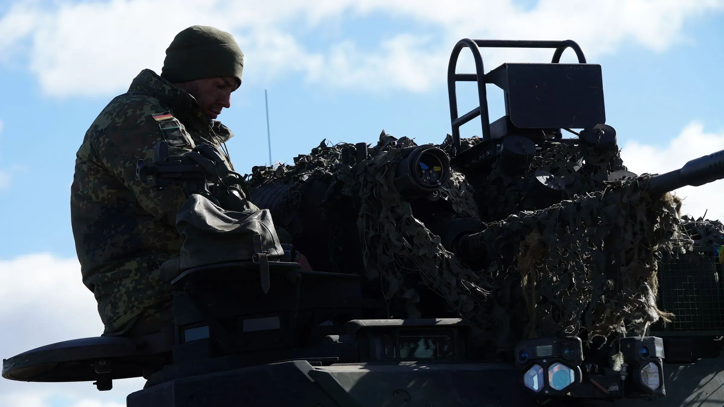 جندي ألماني يجلس على دبابة، يرتدي زيًا عسكريًا ويظهر التركيز أثناء التدريبات العسكرية، مما يعكس التحول في السياسة الدفاعية لألمانيا.