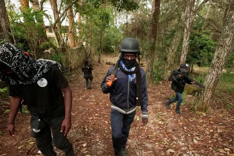 رجال مسلحون يرتدون خوذات وقناع، يتجولون في غابة كثيفة، مما يعكس حالة عدم الأمان والعنف السائد في هايتي.