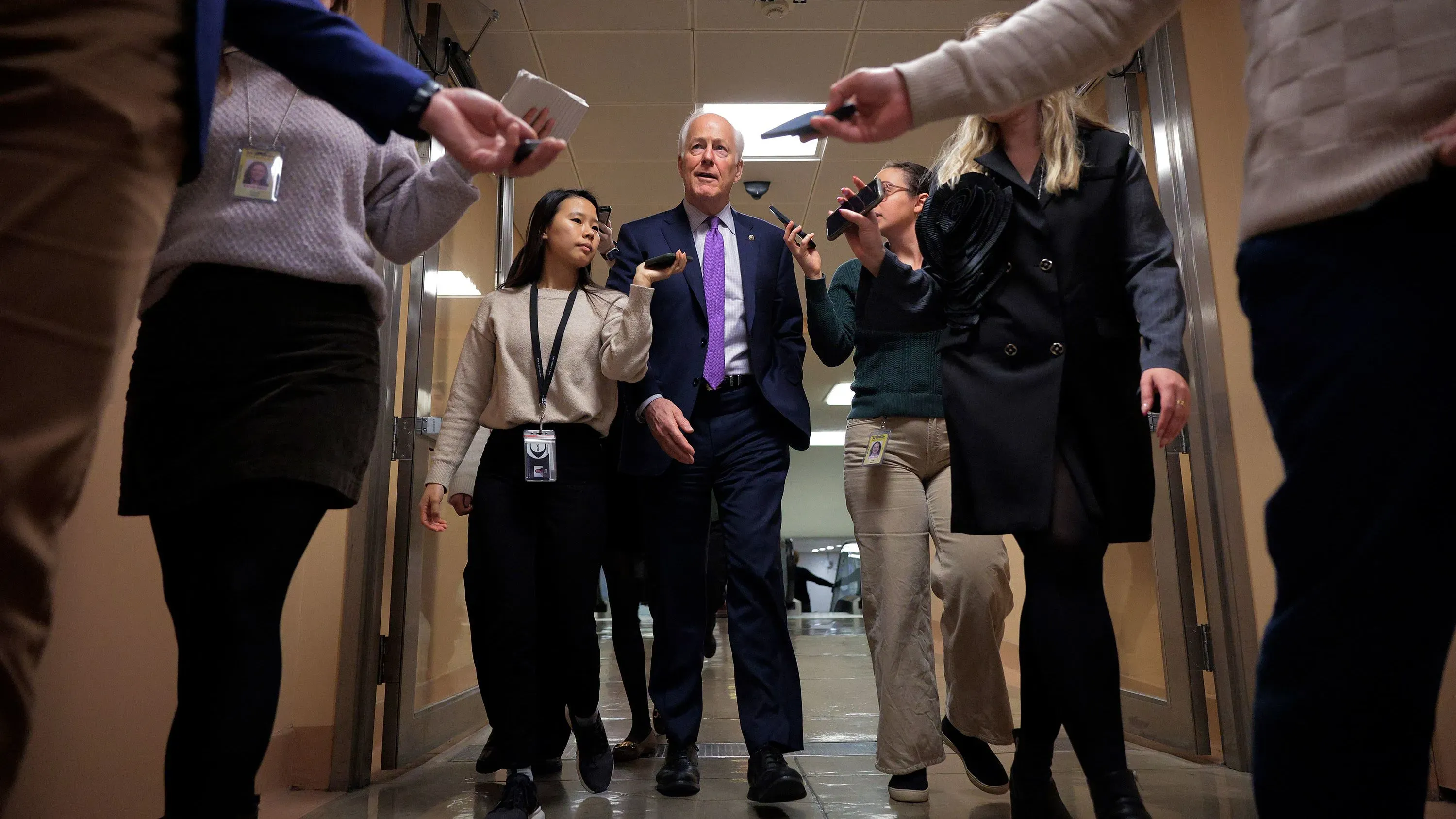 مجموعة من الأشخاص يسيرون في ممر، مع وجود سيناتور وسطهم، حيث يبدو النقاش حول الانتخابات التمهيدية للحزب الجمهوري في تكساس.