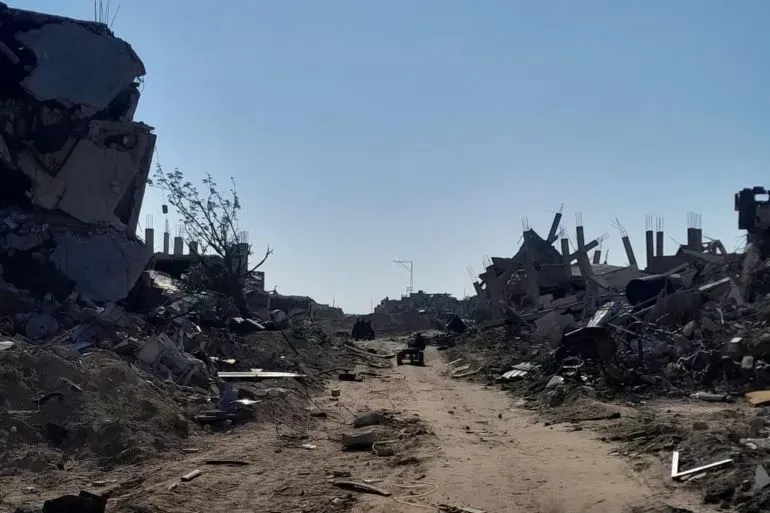 تظهر الصورة مشهدًا مدمّرًا في غزة، حيث تتناثر الأنقاض على جانب الطريق، مما يعكس آثار الحرب والدمار الذي تعرضت له المنطقة.