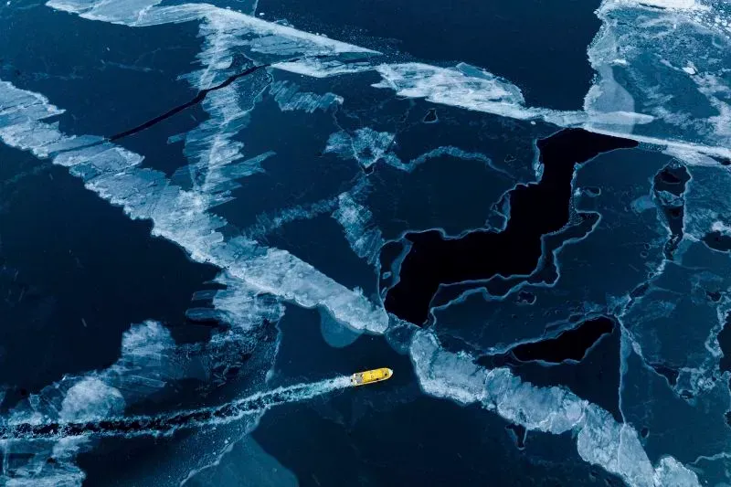 زورق أصفر يبحر عبر مياه جليدية في جرينلاند، محاط بكتل من الجليد، مما يعكس جمال الطبيعة القطبية ويعزز السياحة في المنطقة.