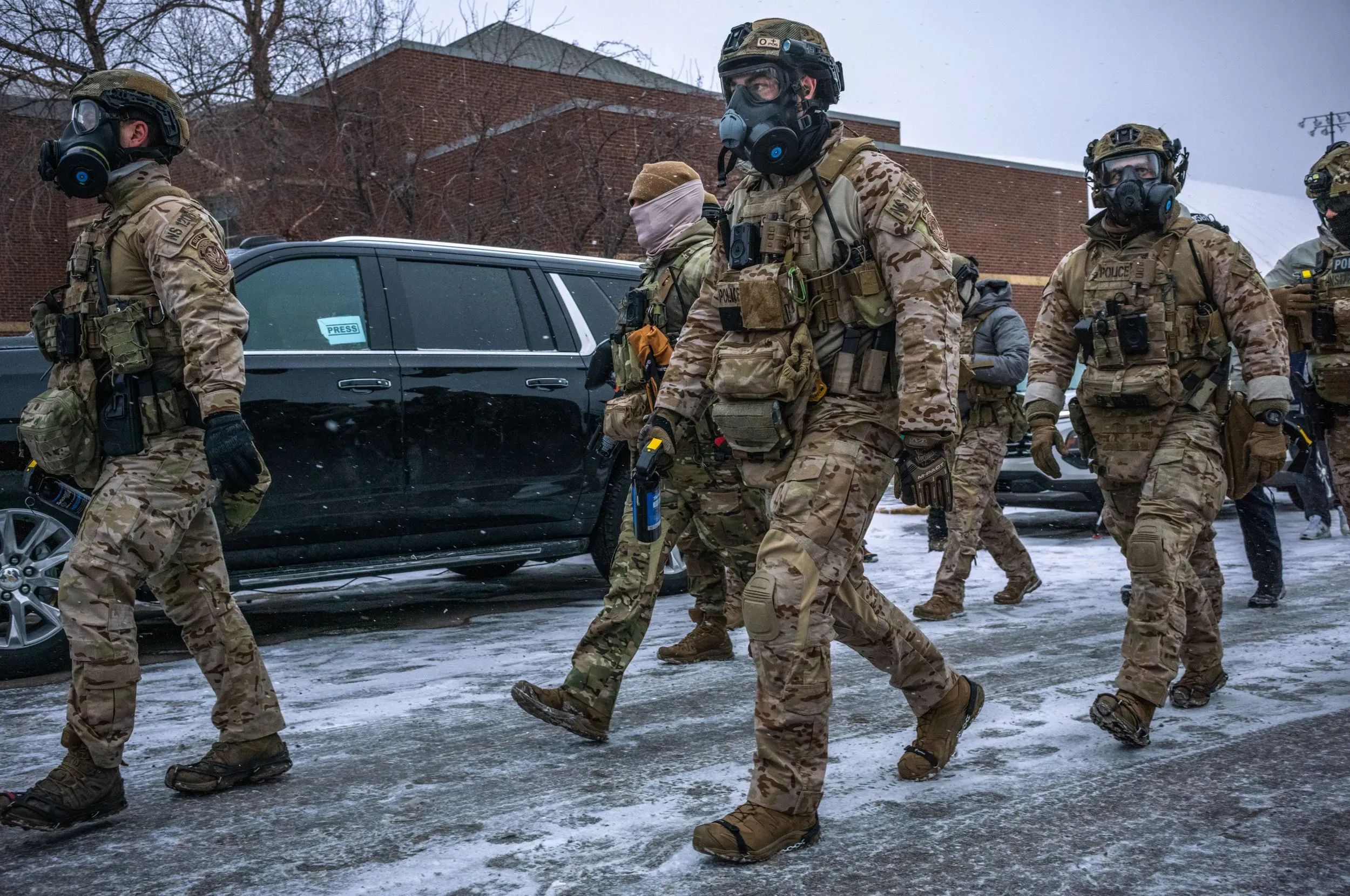 عناصر من القوات الفيدرالية المسلحة يرتدون زيًا عسكريًا وأقنعة واقية، يسيرون في شوارع مينيابوليس المغطاة بالثلوج، وسط أجواء مشحونة.