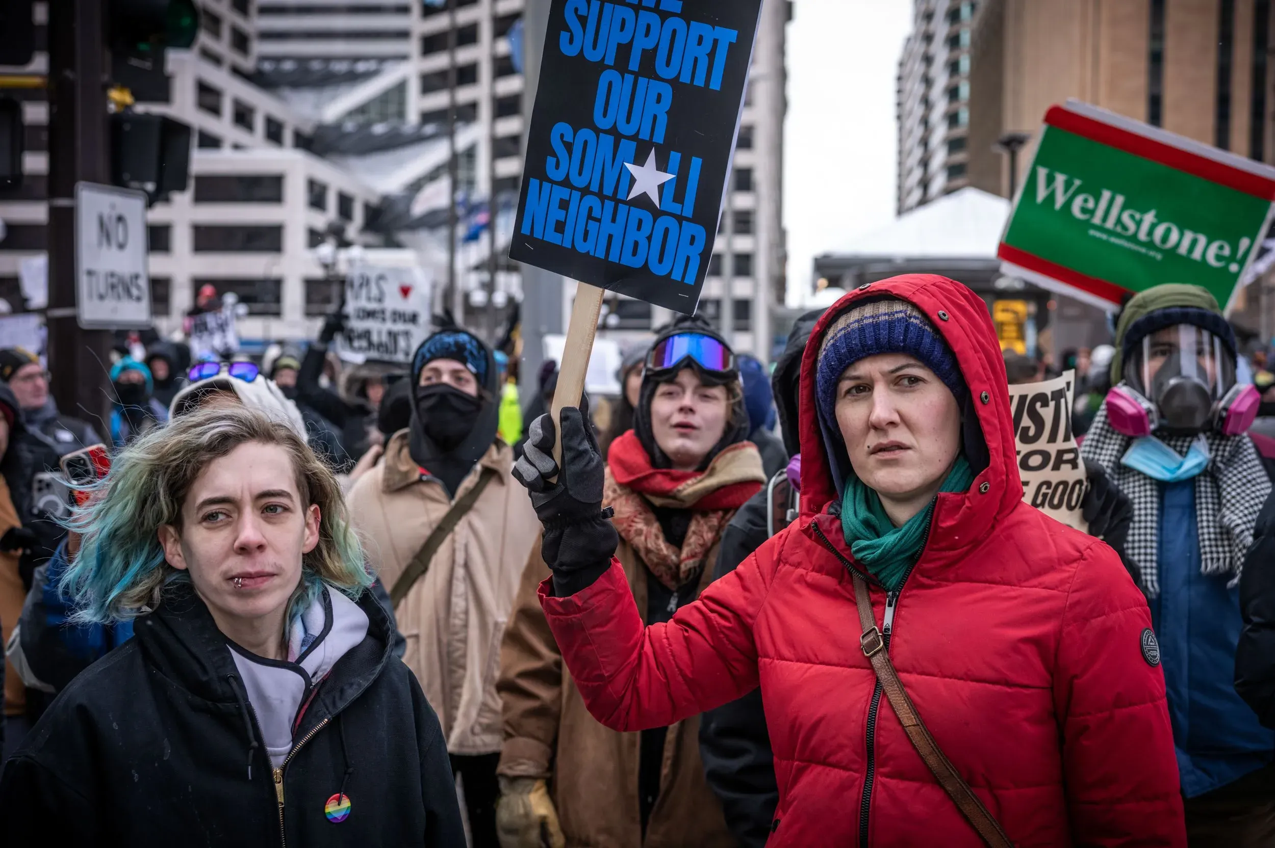 محتجون في مينيابوليس يحملون لافتات تدعو لدعم الجيران، مع التركيز على القضايا الاجتماعية والعدالة، في أجواء شتوية باردة.