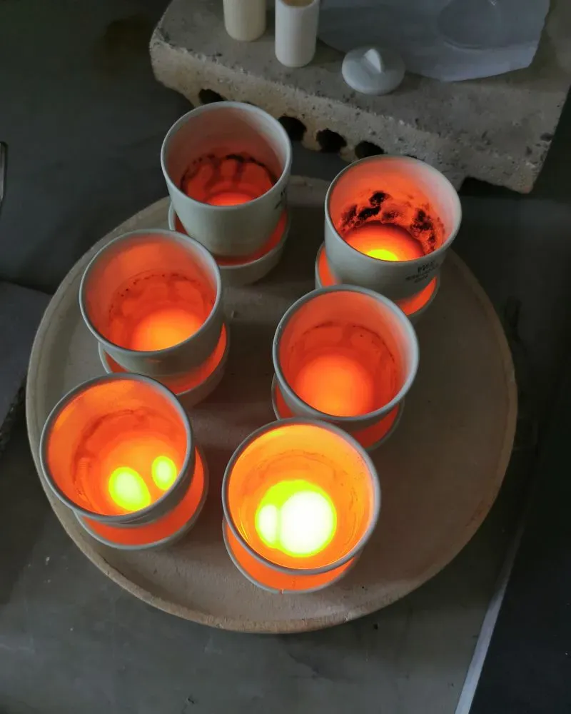 أوانٍ حرارية تحتوي على صخور منصهرة، تتوهج بألوان برتقالية وخضراء، تعكس دراسة المعادن الثمينة من لب الأرض.