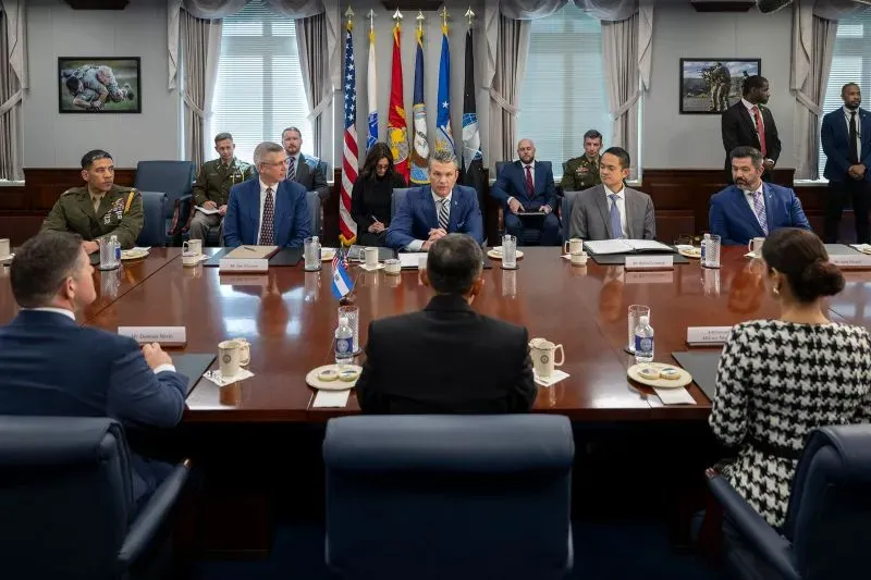اجتماع في وزارة الدفاع الأمريكية، حيث يجلس عدد من المسؤولين العسكريين والمدنيين حول طاولة، مع العلم الوطني خلفهم.
