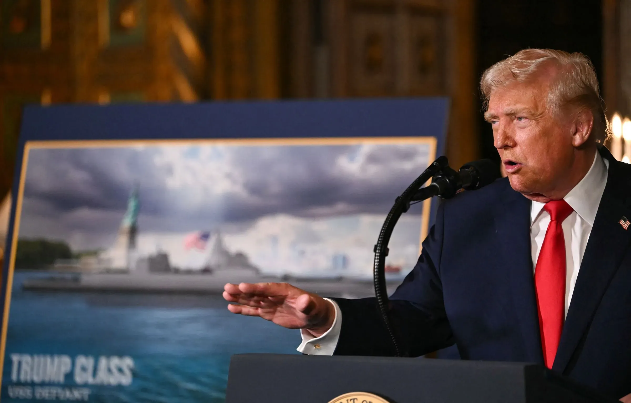 ترامب يتحدث في حدث للإعلان عن سفن "فئة ترامب" الجديدة، مع صورة خلفه تظهر تصميم السفينة.