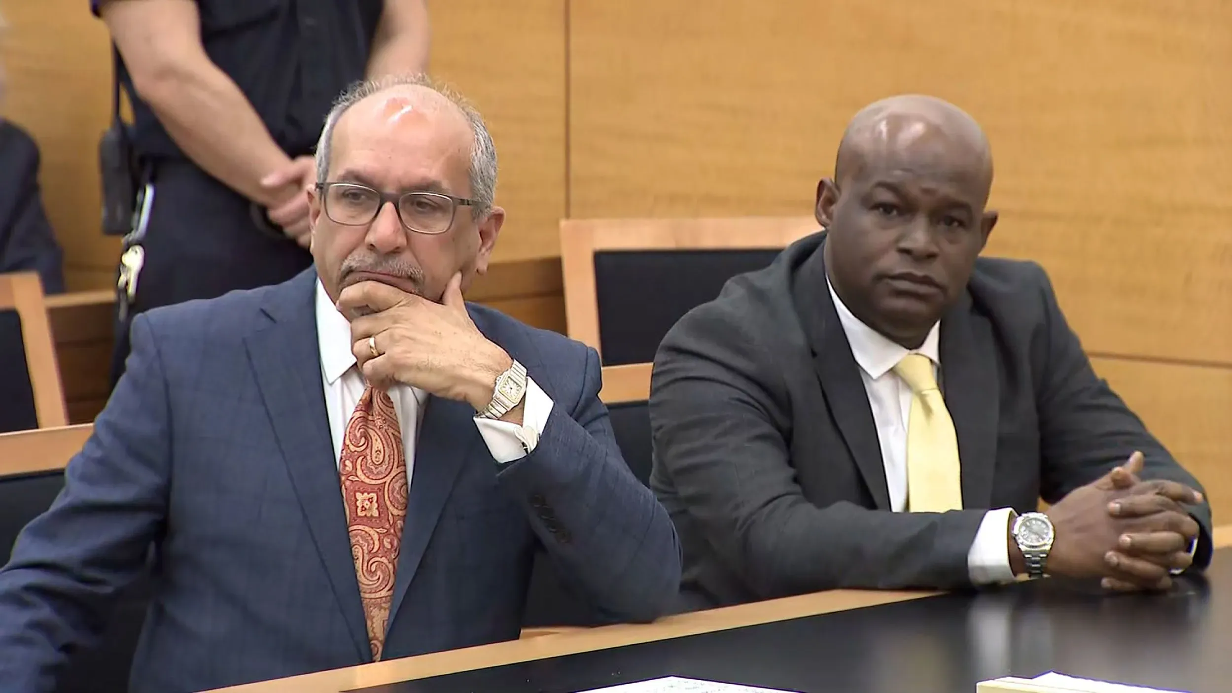 صورة لمشهد من قاعة المحكمة حيث يجلس محامٍ ورجل آخر، مع التركيز على تعابير الوجوه الجادة، تعكس التوتر في قضية إيميل ماكدويل.