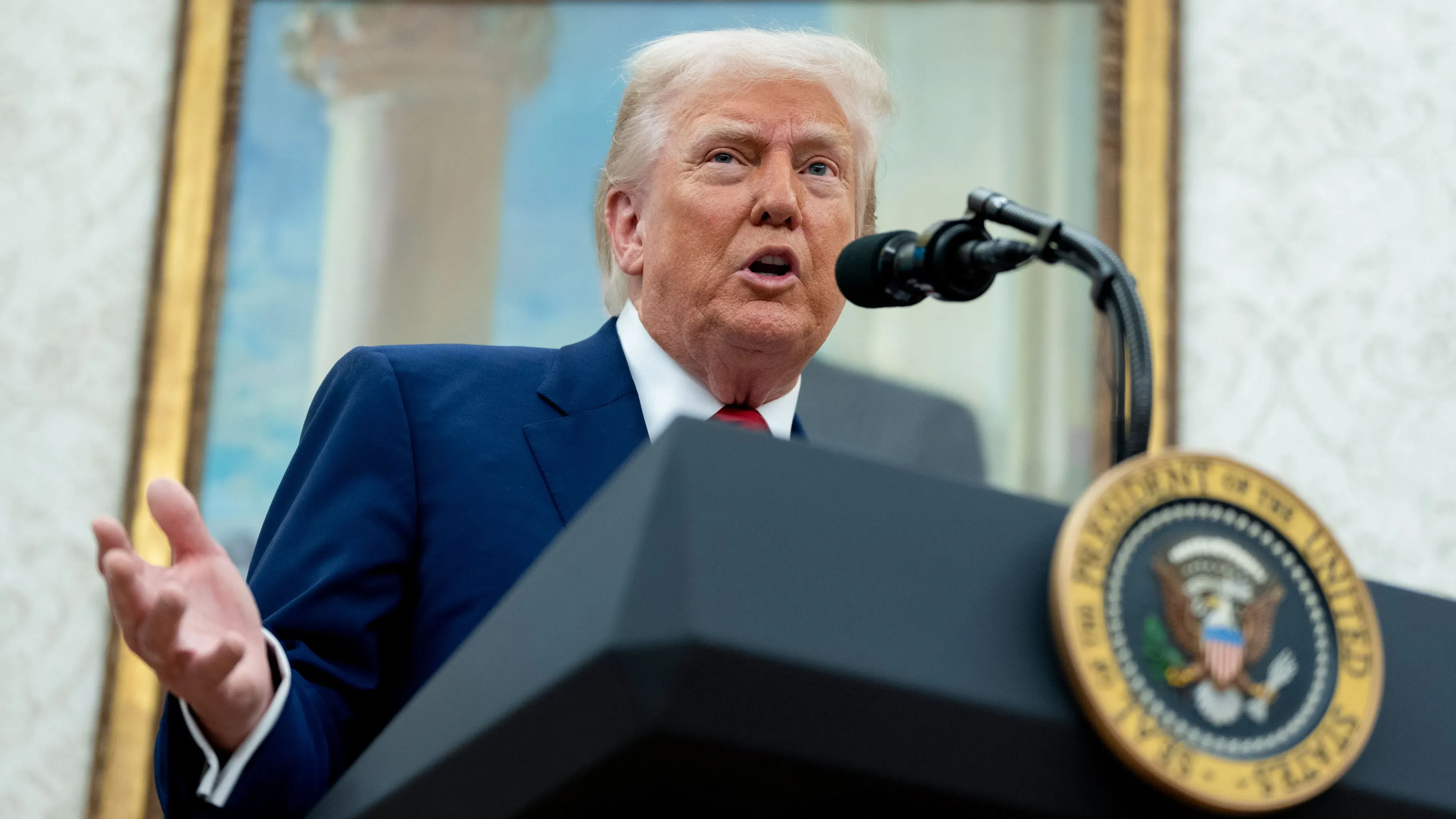 الرئيس ترامب يتحدث من خلف منصة في المكتب البيضاوي، مع تعبير وجهه يظهر الإحباط، بينما يتناول التعريفات الجمركية.