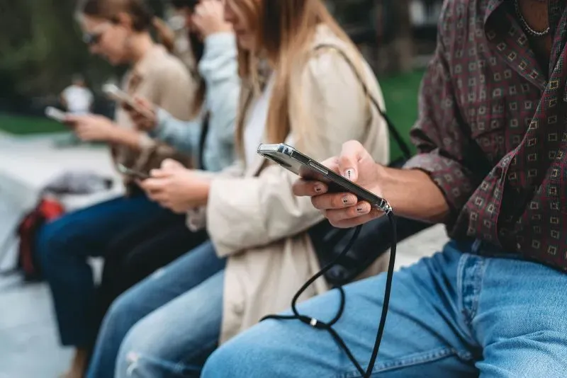 مجموعة من الأشخاص يجلسون في حديقة، كل منهم يستخدم هاتفه الذكي، مما يعكس تأثير وسائل التواصل الاجتماعي على المعلومات الصحية.