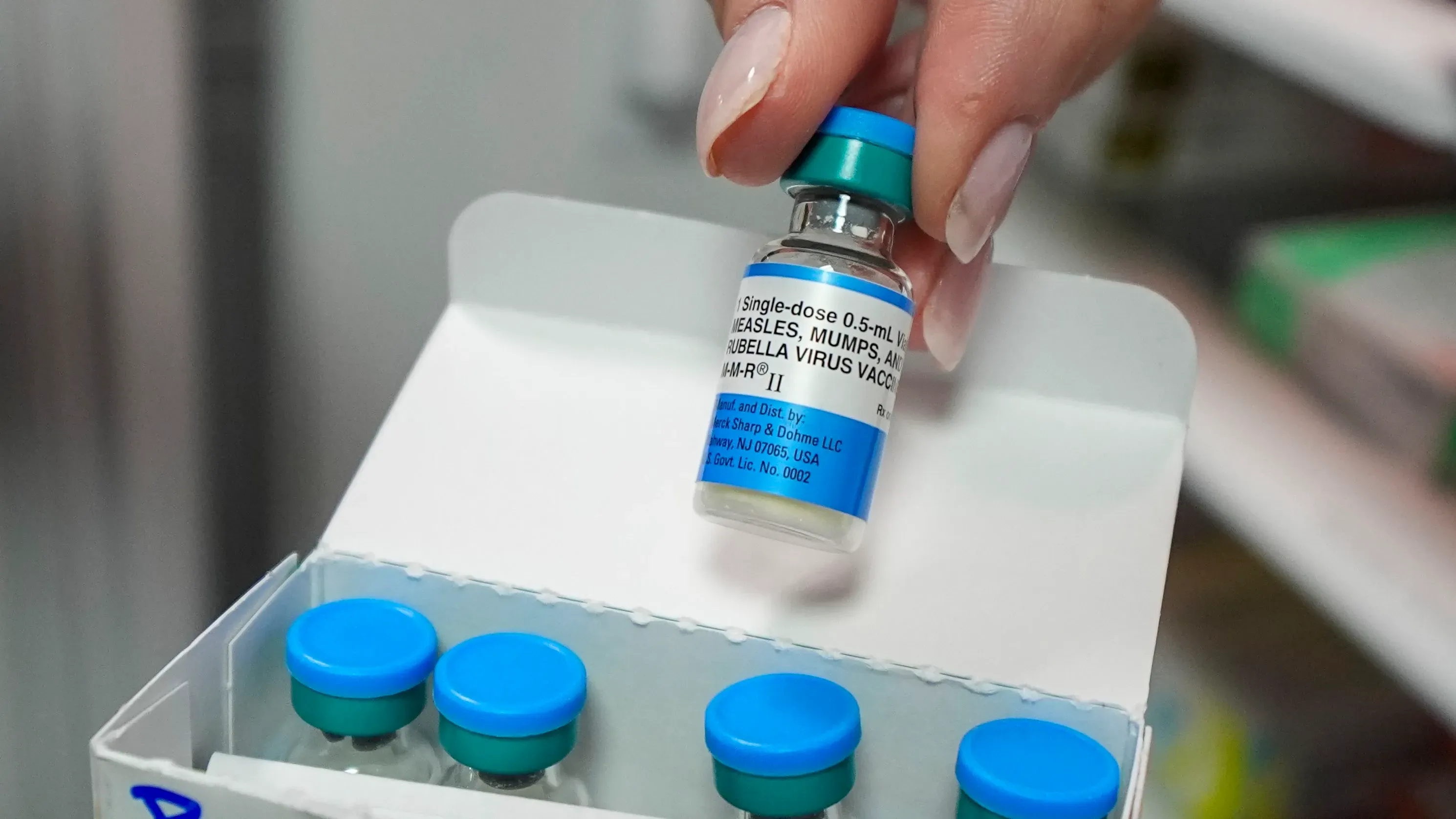 زجاجة لقاح ضد الحصبة والنكاف والحصبة الألمانية، مع وجود أمبولات ملونة في الخلفية، تشير إلى جهود التطعيم في تكساس.