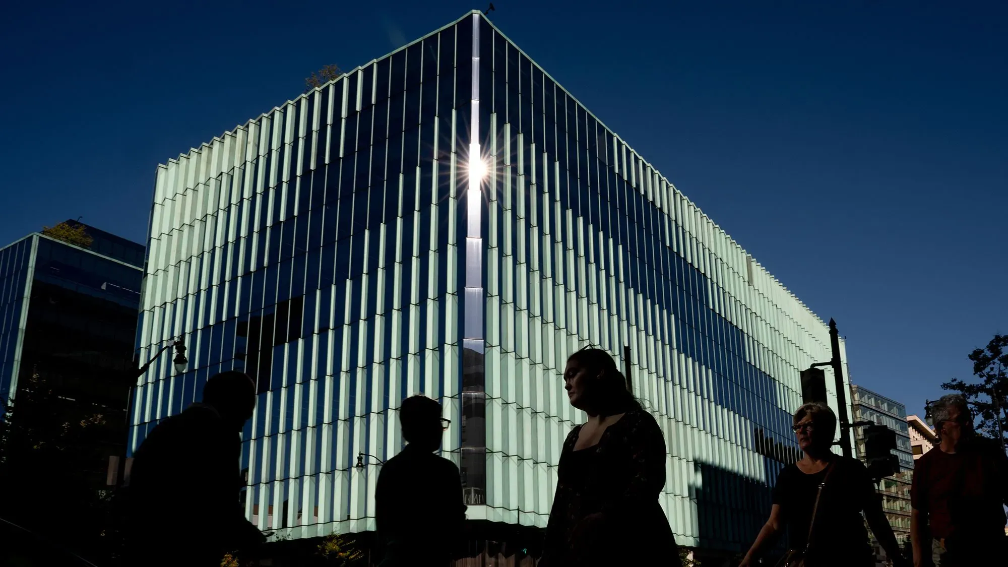 مبنى زجاجي عصري يعكس أشعة الشمس، مع silhouettes لأشخاص يمشون أمامه، يعكس النشاط الاقتصادي في سوق الرهن العقاري الأمريكي.