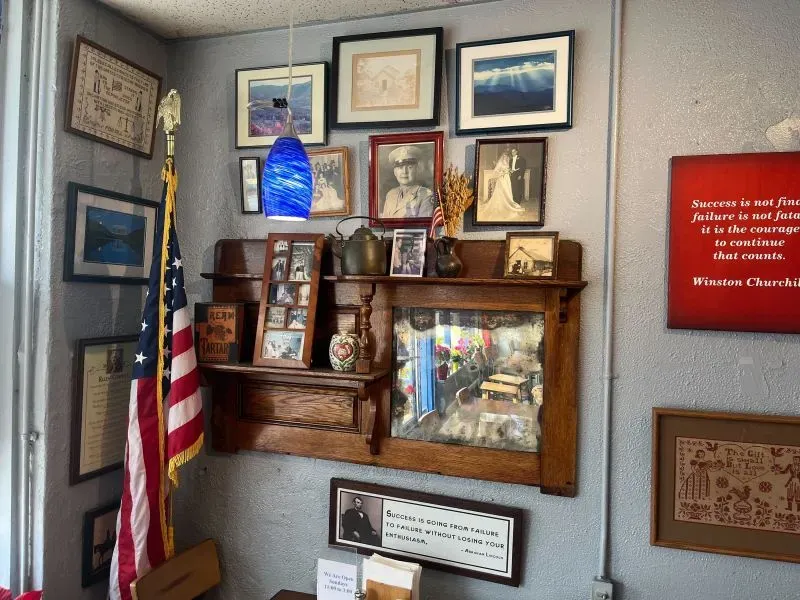 جدار مزين بصور عائلية وشهادات، مع لافتة تحفيزية لوينستون تشرشل، وعلم أمريكي، يعكس روح الأمل والتفاؤل في مطعم روجرز.