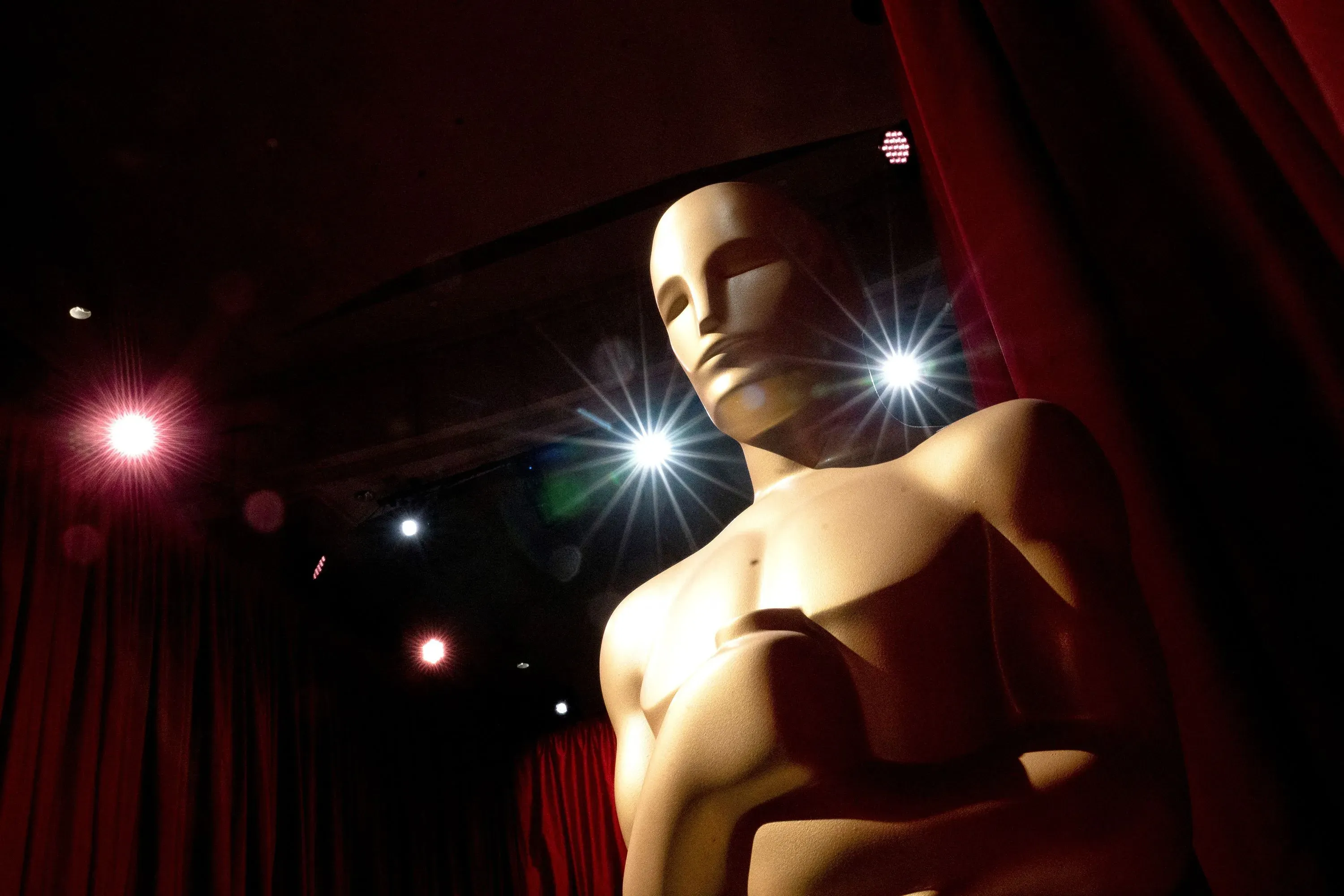 تمثال الأوسكار يضيء تحت الأضواء الساطعة، محاطًا بستائر حمراء، في إطار يرمز لاحتفالية جوائز الأوسكار.