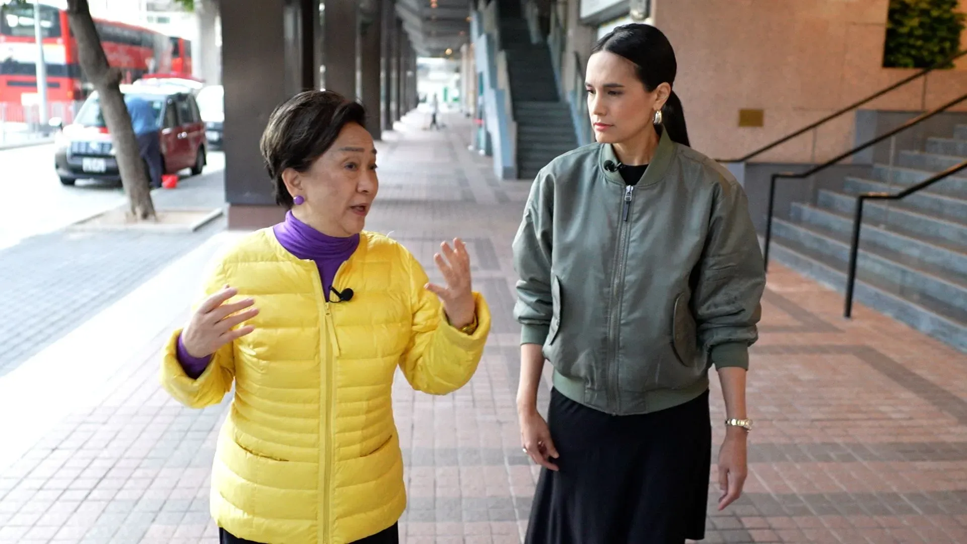 امرأتان تتحدثان في شارع حضري، واحدة ترتدي سترة صفراء والأخرى سترة رمادية، تعكسان أجواء النقاش حول الوضع السياسي في هونغ كونغ.