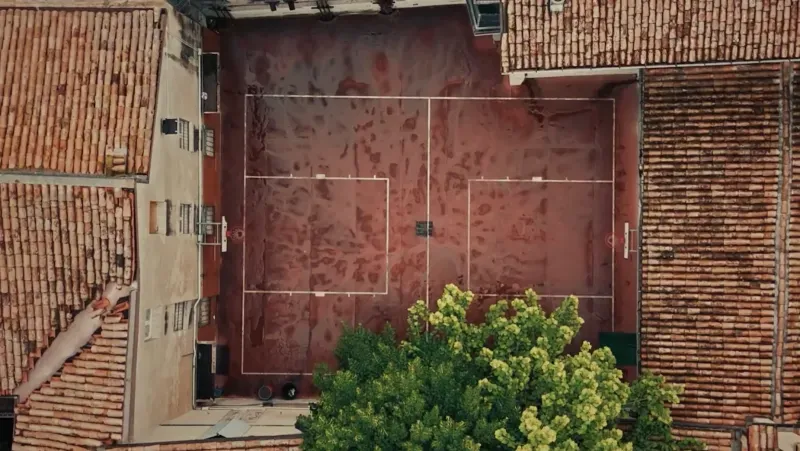 ملعب كرة سلة بسيط في مدينة ريجيو إيميليا الإيطالية، يظهر فيه السطح المهترئ ومحاط بمبانٍ تاريخية وأشجار.