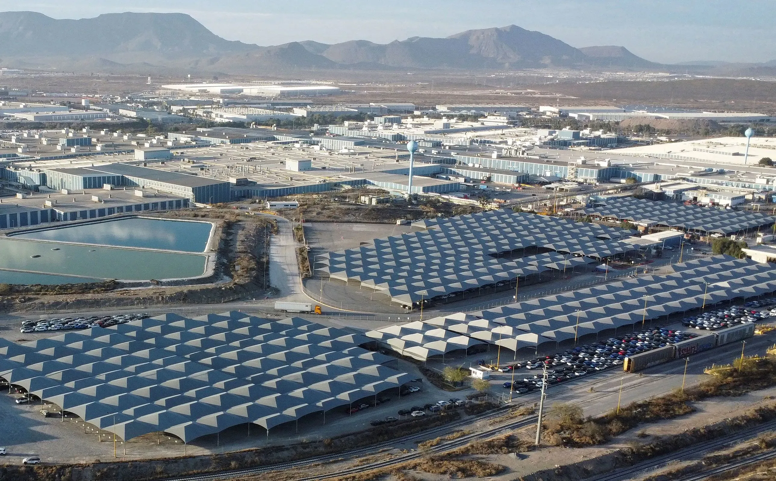 صورة جوية لمصنع كبير في المكسيك، يظهر فيه مواقف سيارات مظللة ومرافق صناعية، تعكس تأثير الحرب التجارية على الشركات.