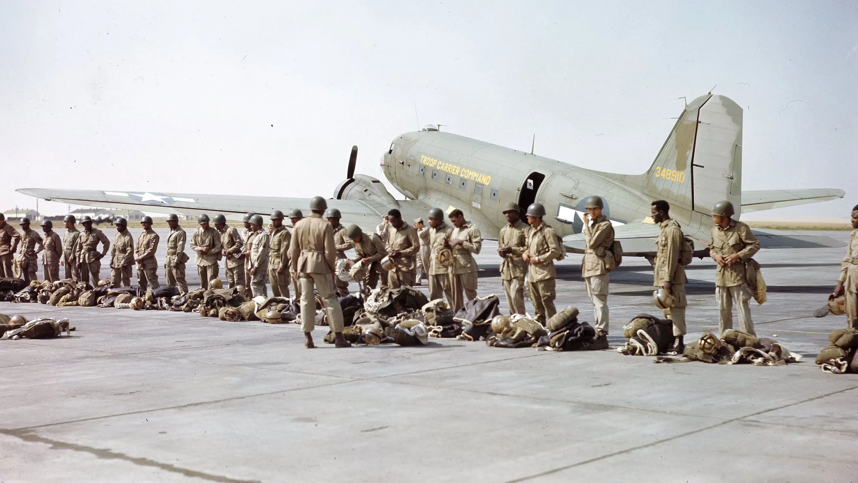 مجموعة من الجنود يرتدون زيًا عسكريًا يتجمعون أمام طائرة من حقبة الحرب العالمية الثانية، مستعدين للقفز بالمظلات في مهمة إطفاء حرائق الغابات.