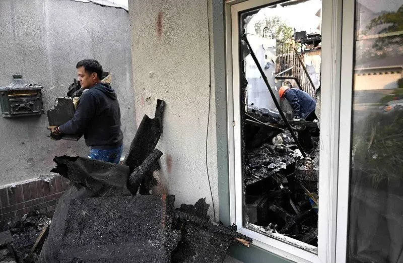 عمال يقومون بإزالة الحطام من منزل دمرته الحرائق، مع وجود آثار الدمار واضحة، مما يعكس حجم الكارثة في لوس أنجلوس.
