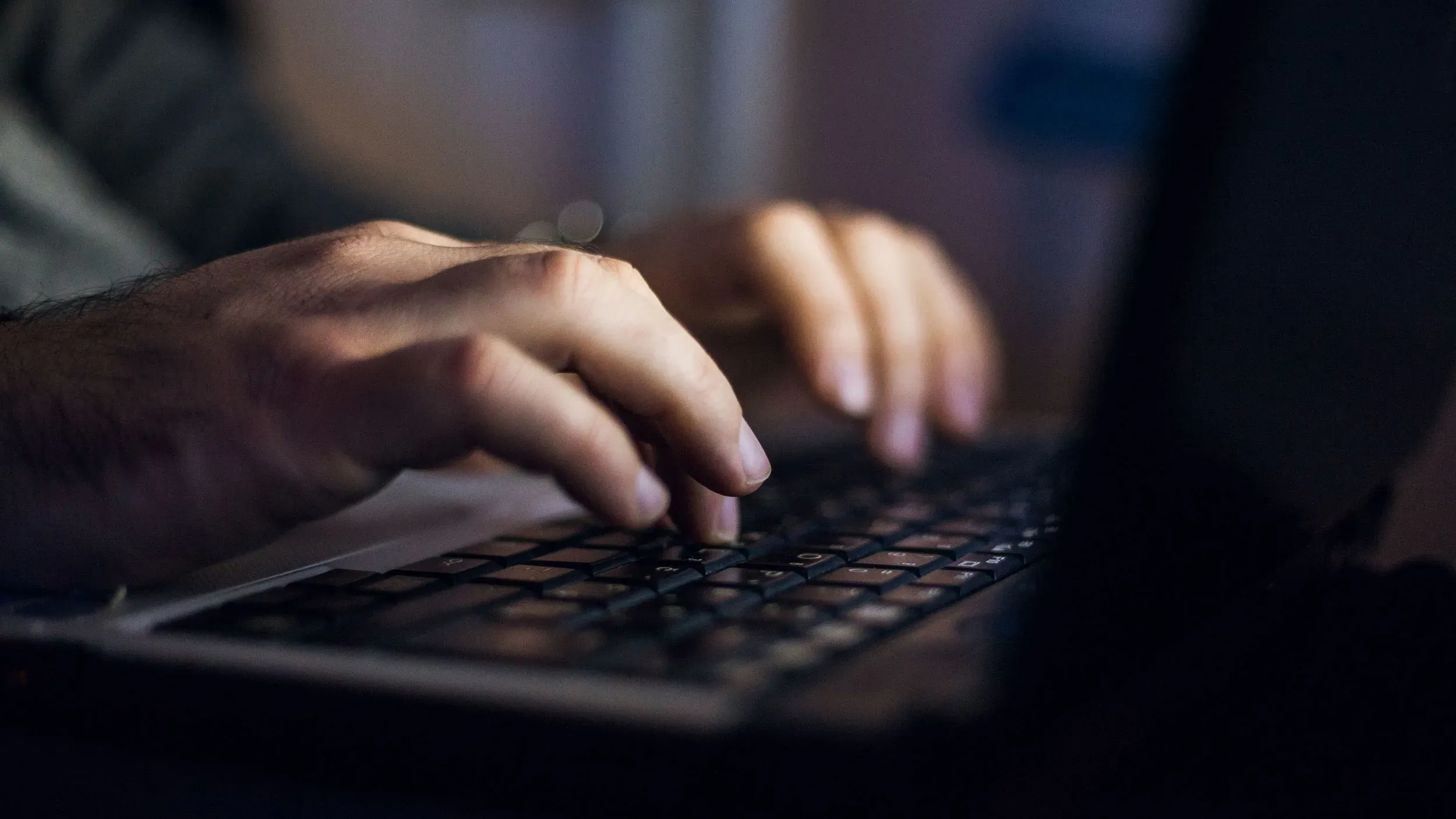 أيدي شخص تكتب على لوحة مفاتيح في بيئة مظلمة، مما يعكس تأثير الإنترنت على خطاب الكراهية والمعلومات المضللة.