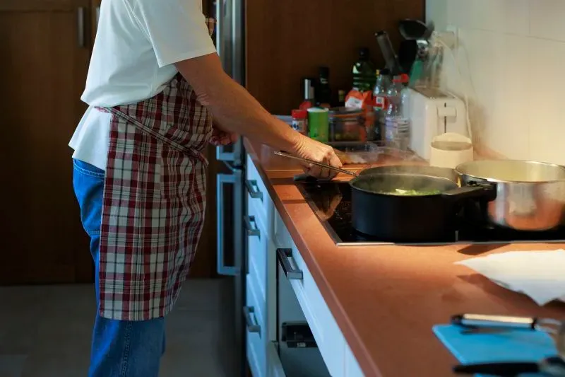 شخص مسن يرتدي مئزرًا ويقوم بالطهي في مطبخ حديث، مما يعكس أهمية الاستقلالية في الحياة اليومية للأشخاص المصابين بالخرف.