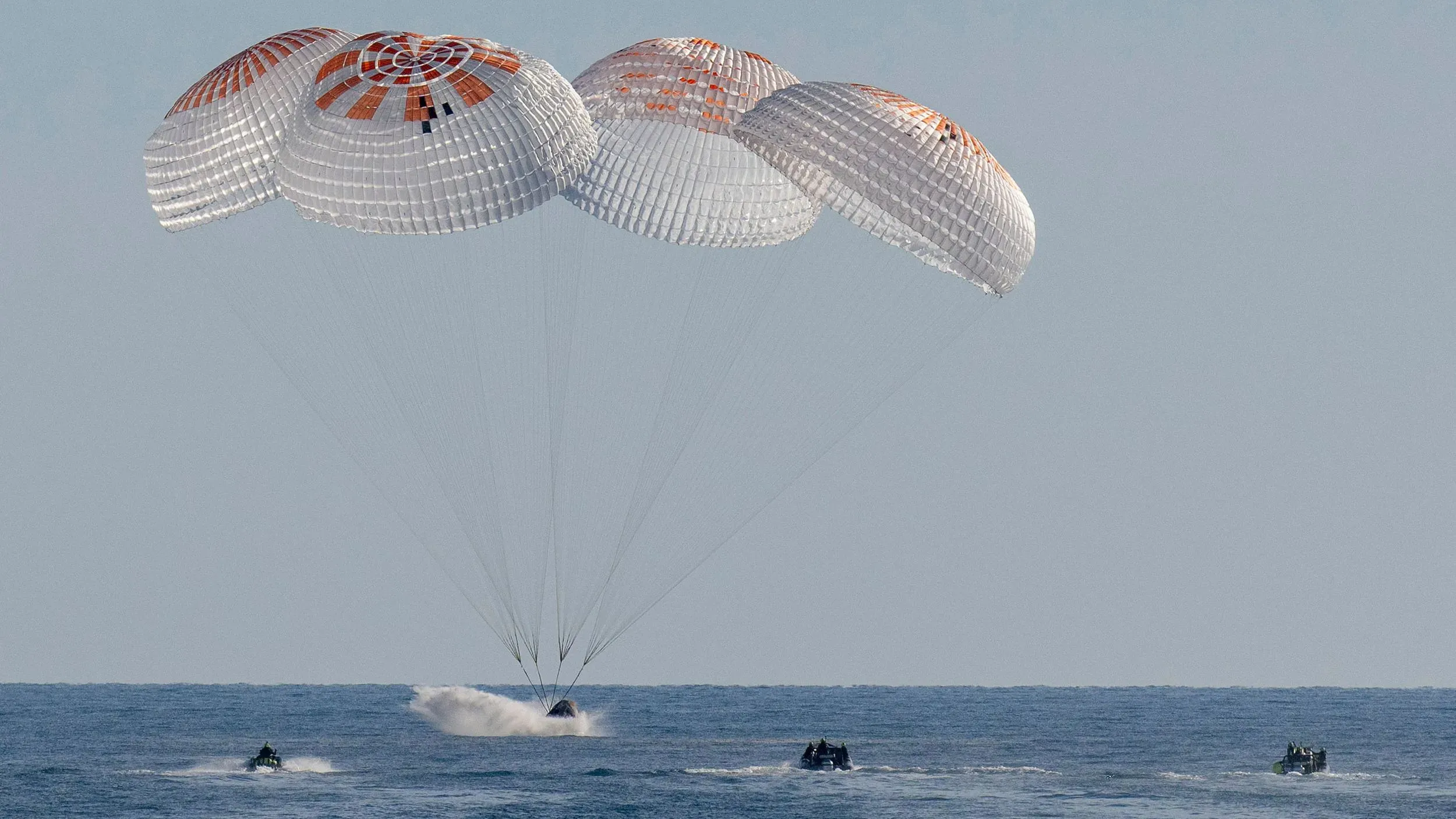 هبوط مركبة فضائية مزودة بمظلات متعددة على سطح الماء، مع قوارب إنقاذ تقترب منها، بعد مهمة طويلة في الفضاء.