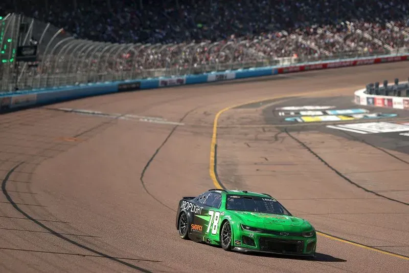 سيارة سباق خضراء من طراز شيفروليه 78 تتسابق على حلبة ناسكار، مع جمهور كبير في الخلفية، تعكس تحديات كاثرين ليج في عالم السباقات.