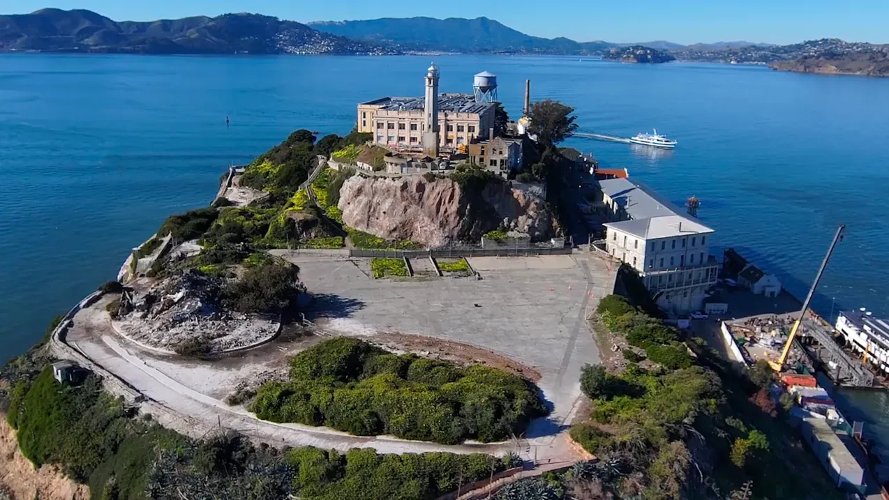 جزيرة الكاتراز تظهر من منظور جوي، مع المباني التاريخية المحاطة بالمياه الزرقاء، تمثل جهود الحفاظ على هذا المعلم التاريخي.