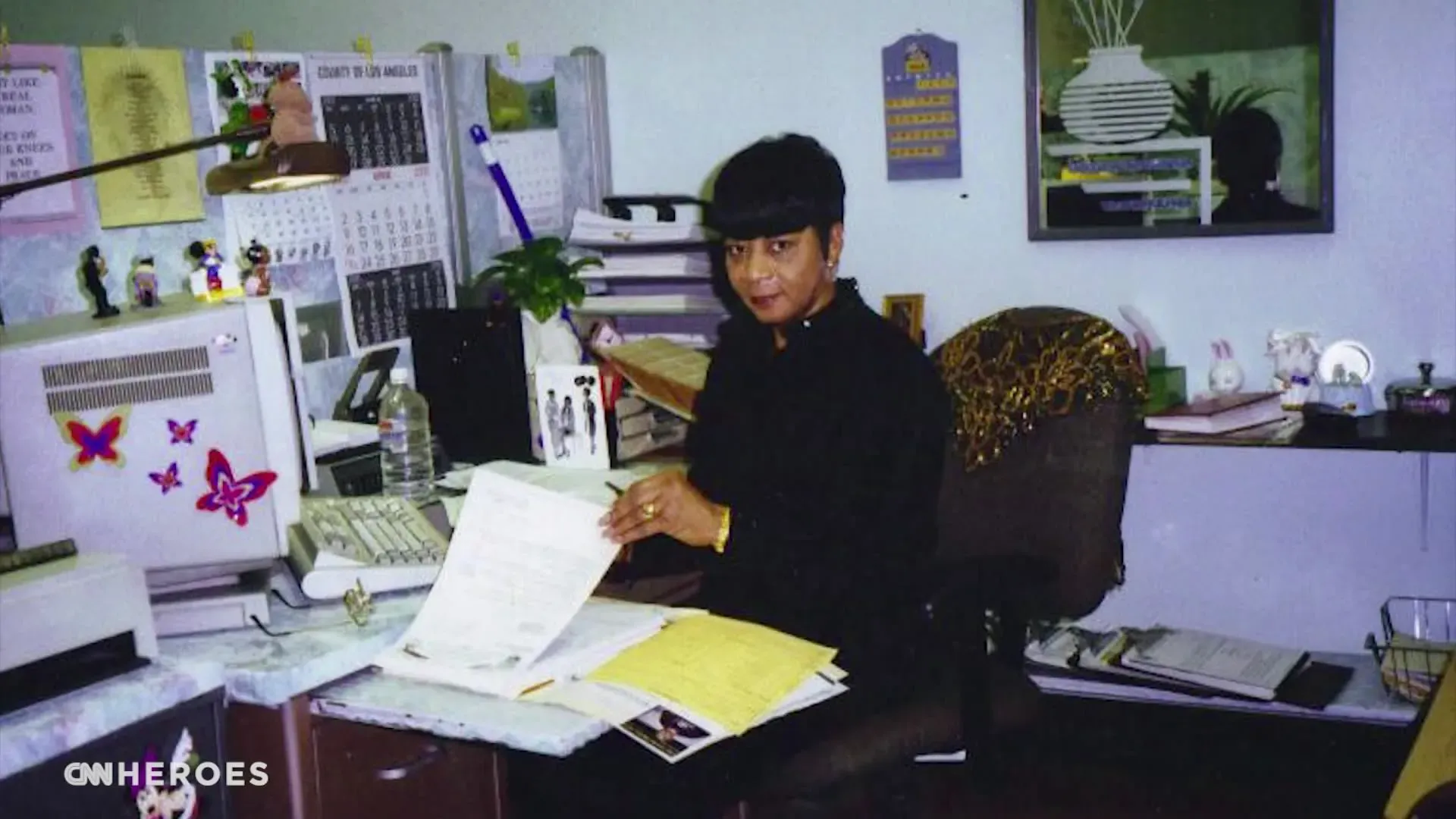 صورة لامرأة تجلس أمام مكتبها، محاطة بأوراق وأدوات مكتبية، تعكس بيئة عمل منظمة.