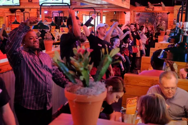 مطعم تكساس رودهاوس يتميز بأجواء حيوية، حيث يشارك الموظفون والزبائن في الاحتفالات، مما يعكس تجربة تناول طعام ممتعة.