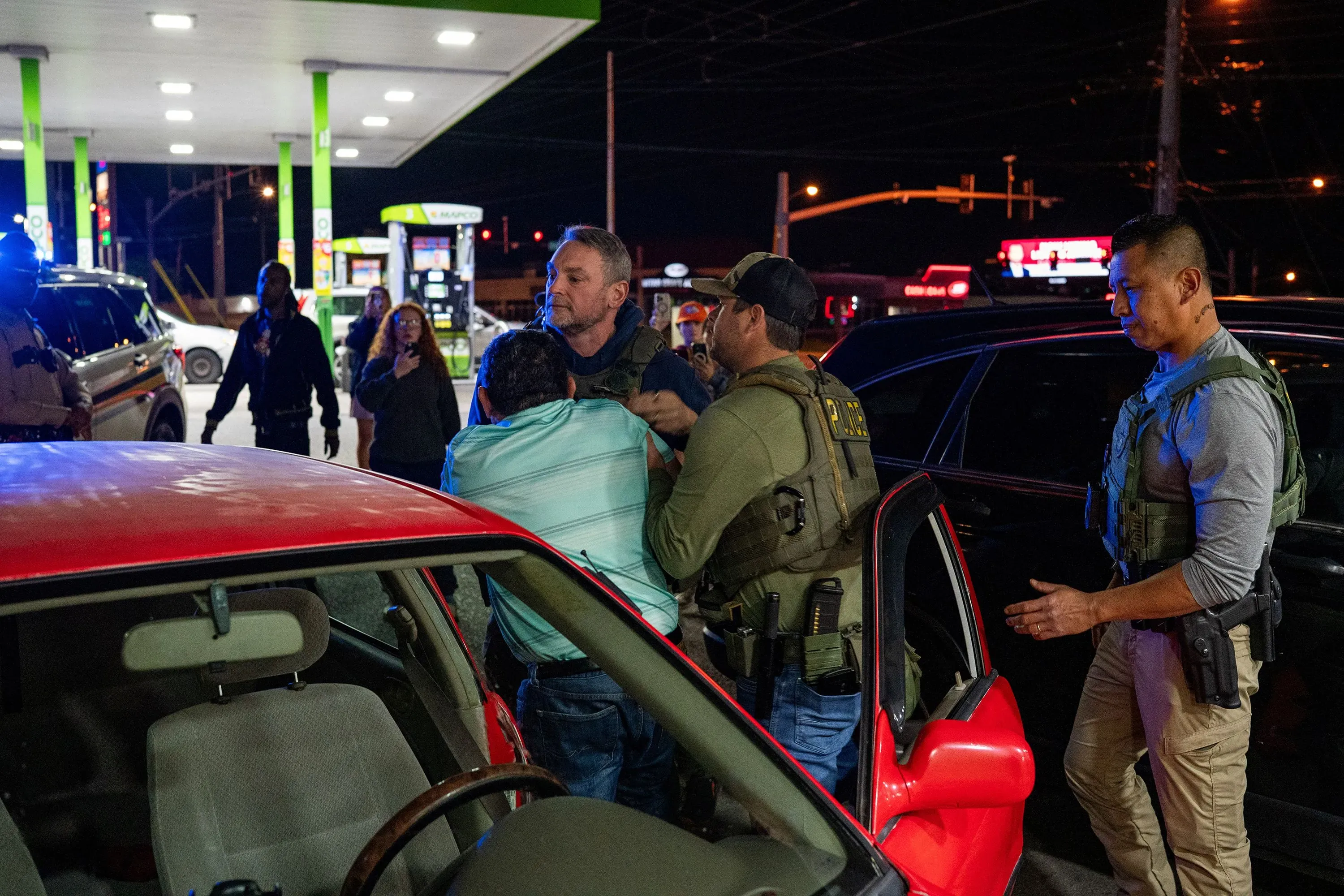 اعتقال شخص في محطة وقود، مع وجود ضباط الشرطة حوله، مما يعكس التوتر الناتج عن حملات الترحيل في الولايات المتحدة.