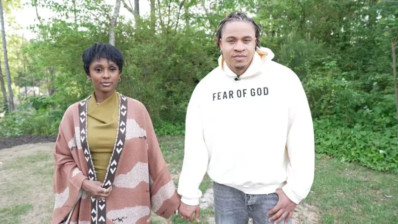 زوجان، روتيمي وفانيسا، يمسكان بأيديهما في بيئة طبيعية، مع التركيز على حبهما العميق وإيمانهما المشترك.