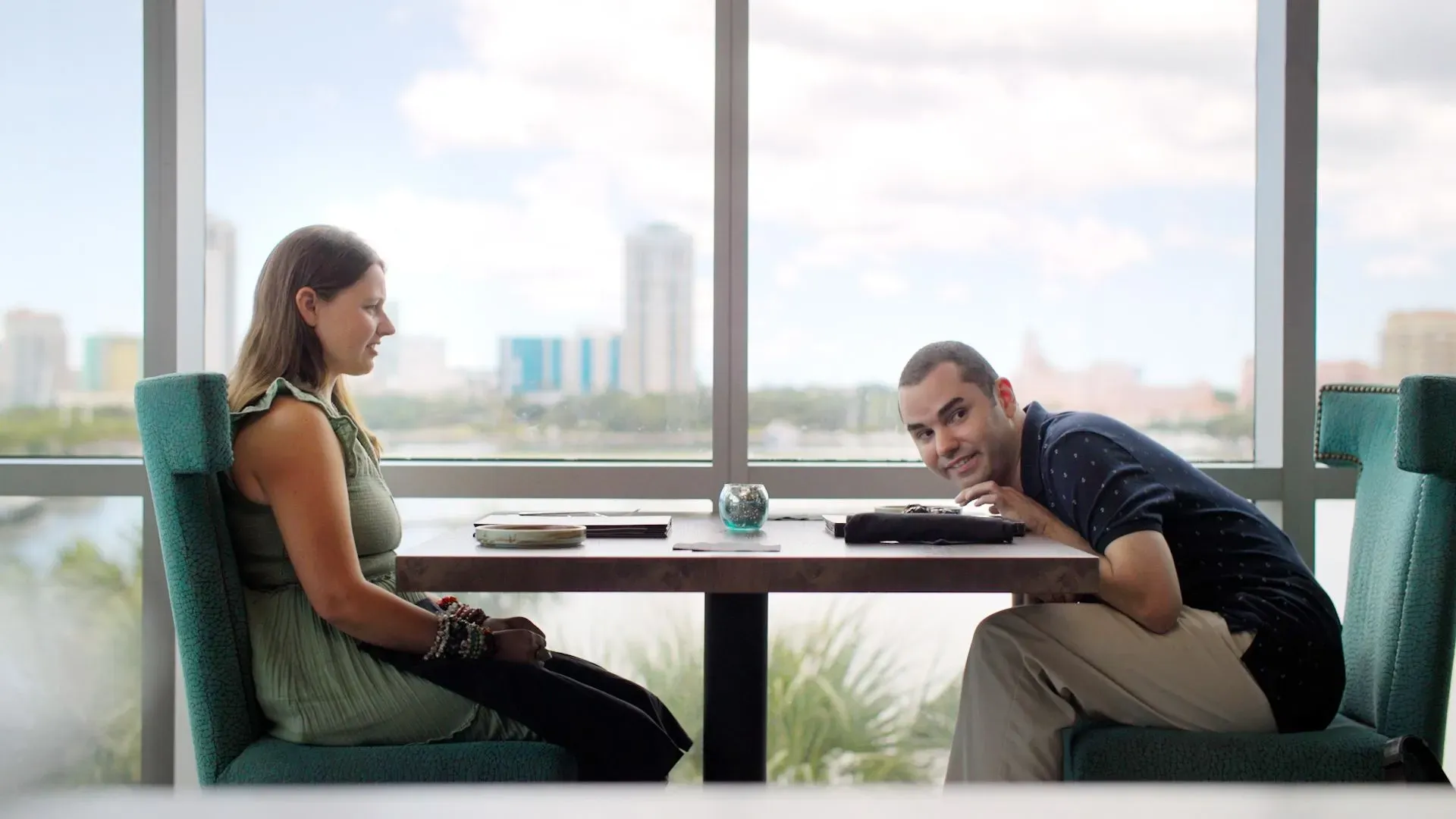 ماديسون ماريلا ورجل يجلسان في مطعم يتحدثان خلال موعد غرامي، مع منظر حضري خلفهما، يعكسان تحديات المواعدة للأشخاص من ذوي التوحد.