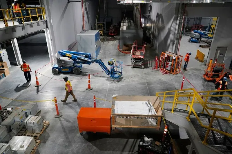 عمال في موقع بناء لمصنع للطاقة المتجددة، مع معدات ومواد في الخلفية، يعكس جهود الصناعة لتعزيز الطاقة النظيفة والوظائف.