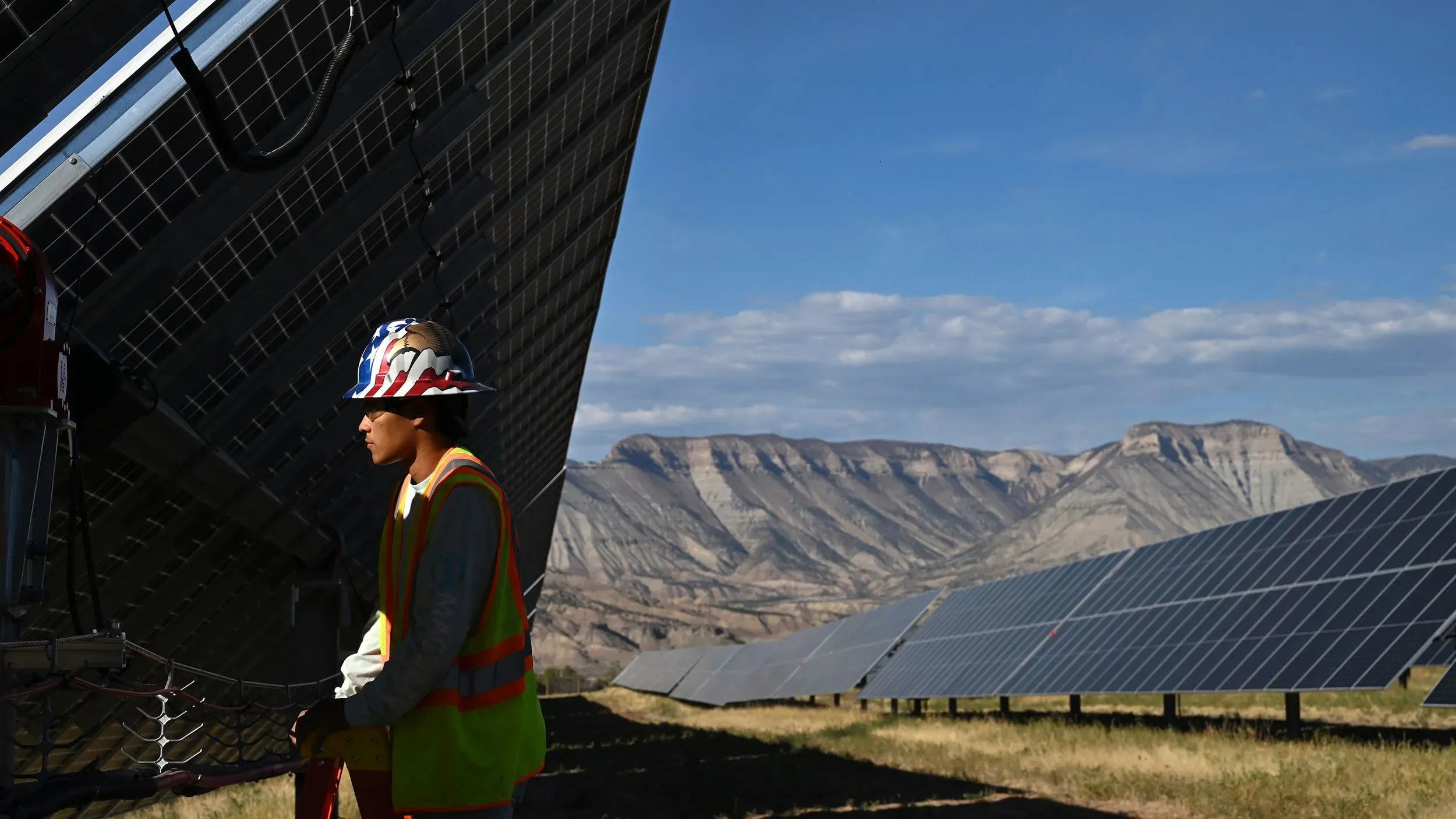 عامل يعمل على تركيب الألواح الشمسية في موقع للطاقة المتجددة، مع مناظر جبلية خلفية، يعكس جهود الصناعة لدعم الطاقة النظيفة.