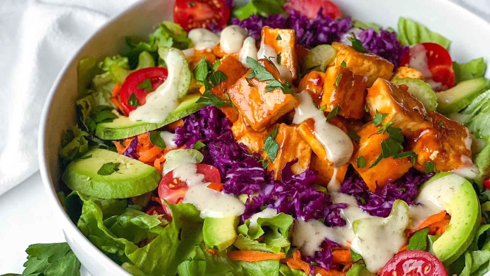 سلطة ملونة تحتوي على خضروات طازجة وتوفو مشوي، مع صلصة كريمية، تعكس أسلوب الحياة النباتي الصحي لجكي أكربيرج.