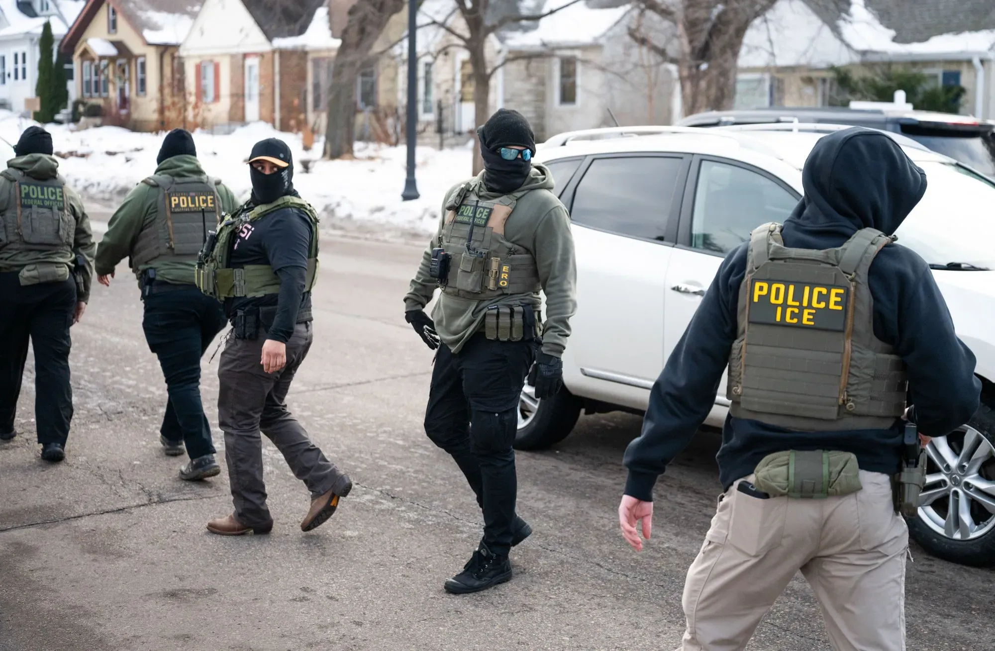 عمليات إنفاذ قوانين الهجرة في مينيابوليس، حيث يظهر ضباط يرتدون سترات واقية ويستعدون لمهمة في منطقة سكنية.