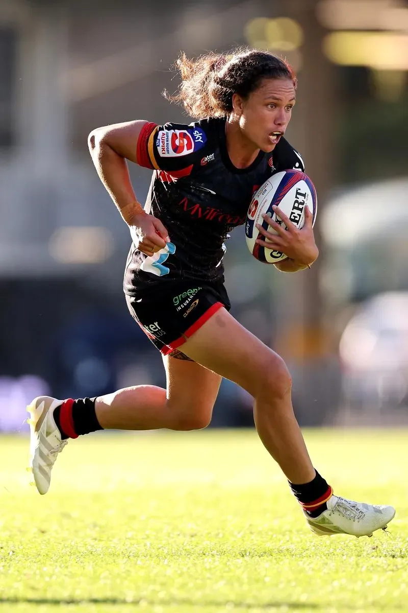 إيلونا ماهر، لاعبة رجبي أمريكية، تجري بسرعة حاملة الكرة في ملعب، تعكس طموحها ونجاحها في الرياضة.