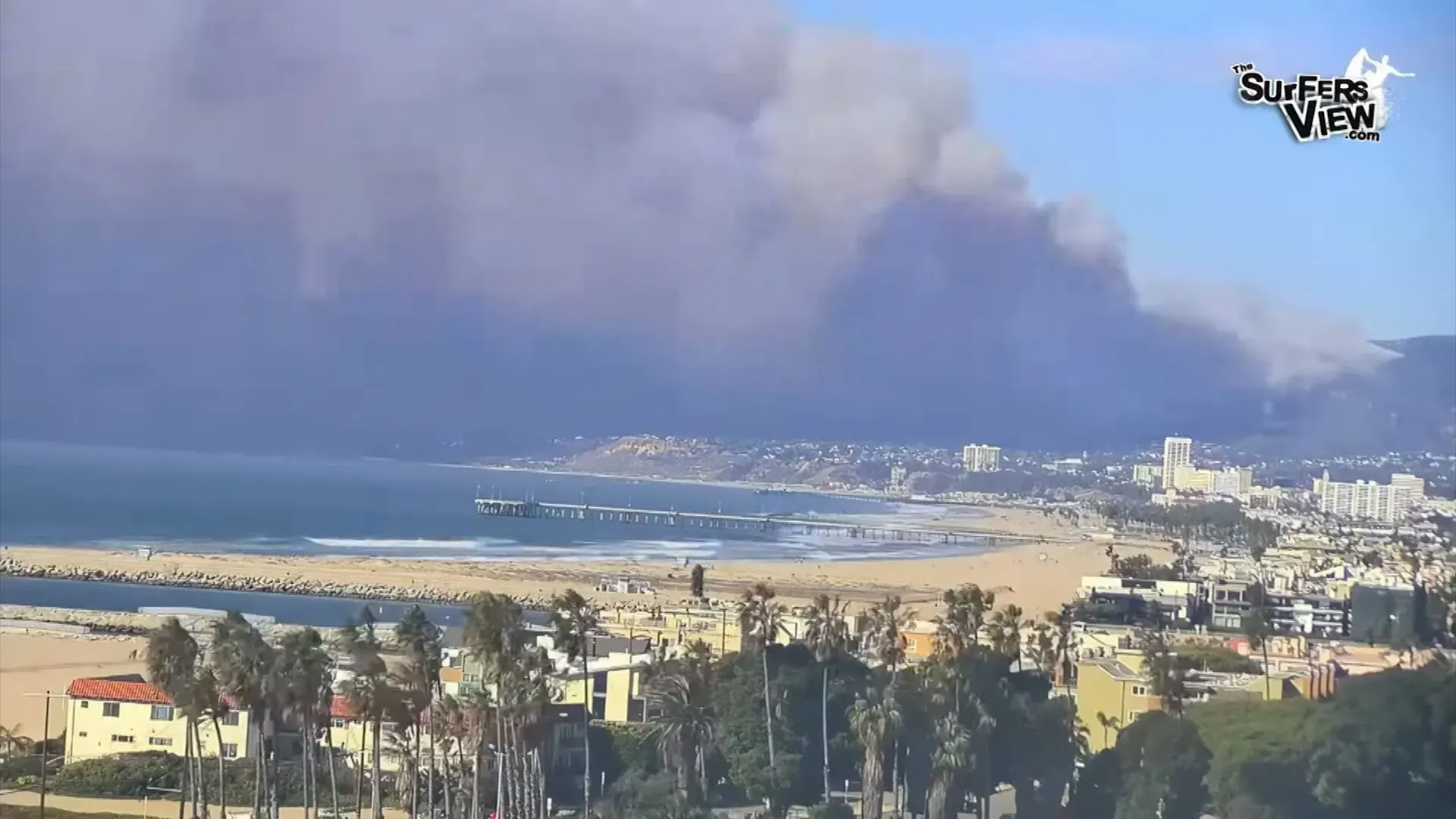 دخان كثيف يغطي السماء فوق شاطئ في كاليفورنيا، حيث تشتعل حرائق الغابات وتدمر المنازل، مما يثير قلق السكان المحليين.