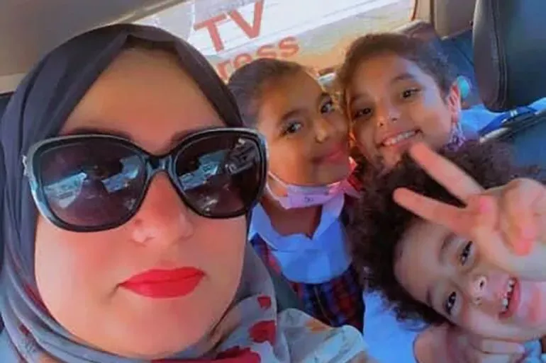 امرأة ترتدي حجابًا مع ثلاثة أطفال في سيارة، يعبرون عن الفرح. تعكس الصورة لحظات عائلية دافئة رغم الظروف الصعبة في غزة.