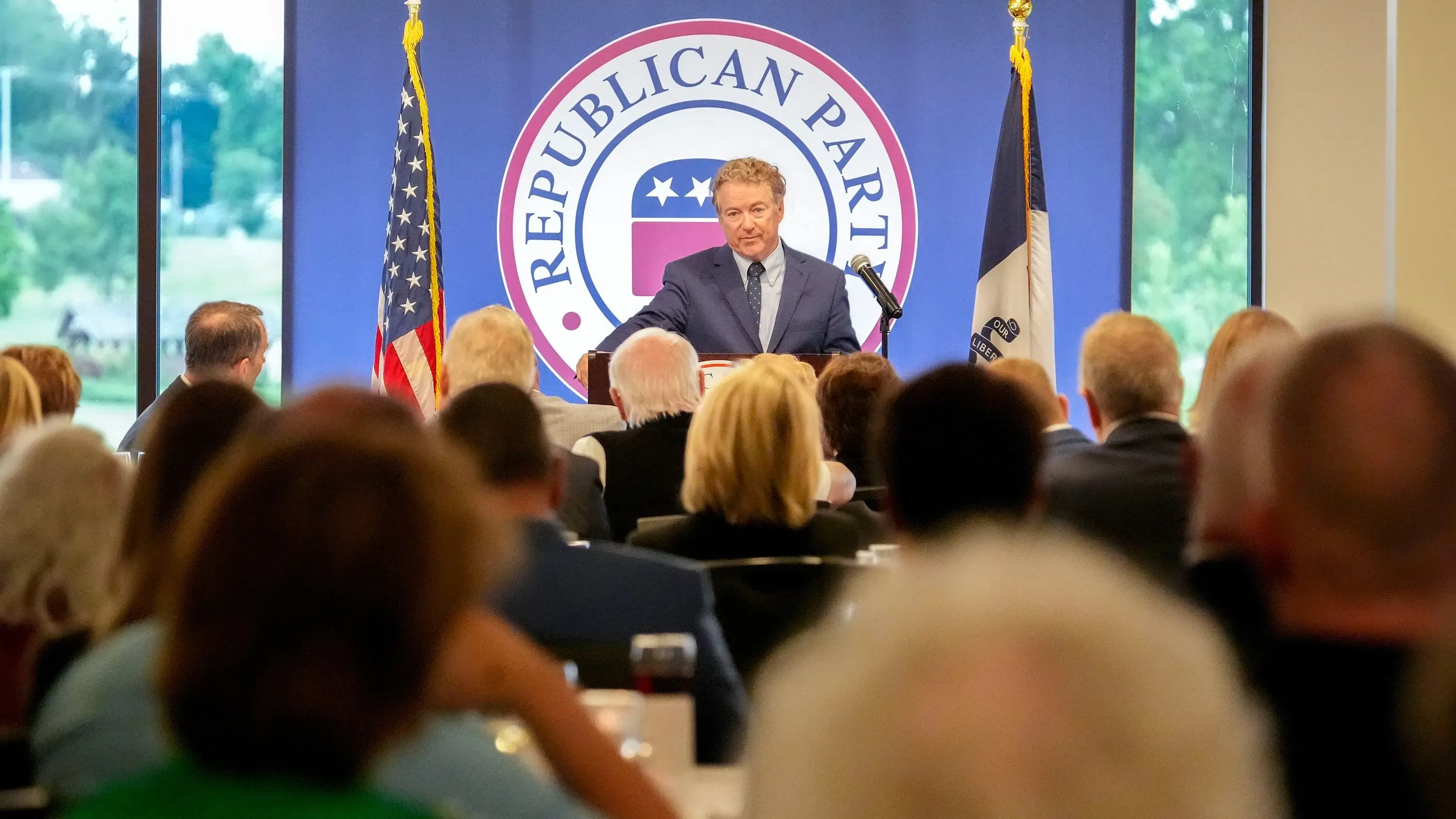 راند بول يتحدث في حدث لجمع التبرعات للحزب الجمهوري في أيوا، مع جمهور من الحضور خلفه، بينما يبرز شعار الحزب.