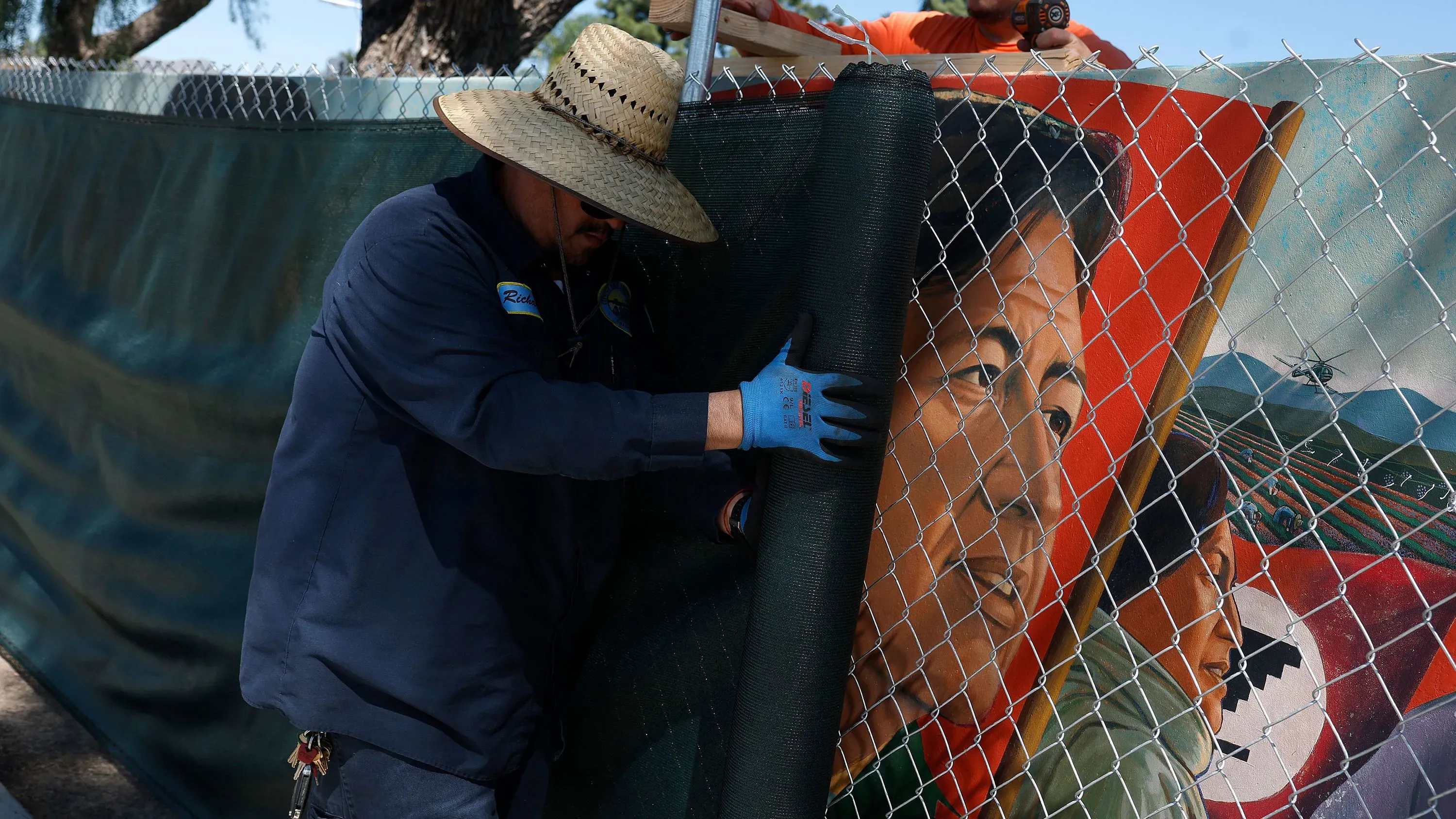 رجل يعمل على تغطية جدارية تصور سيزار تشافيز في سان فرانسيسكو، تعبيرًا عن التغيير في الاحتفاء بإرثه بعد اتهامات جديدة.