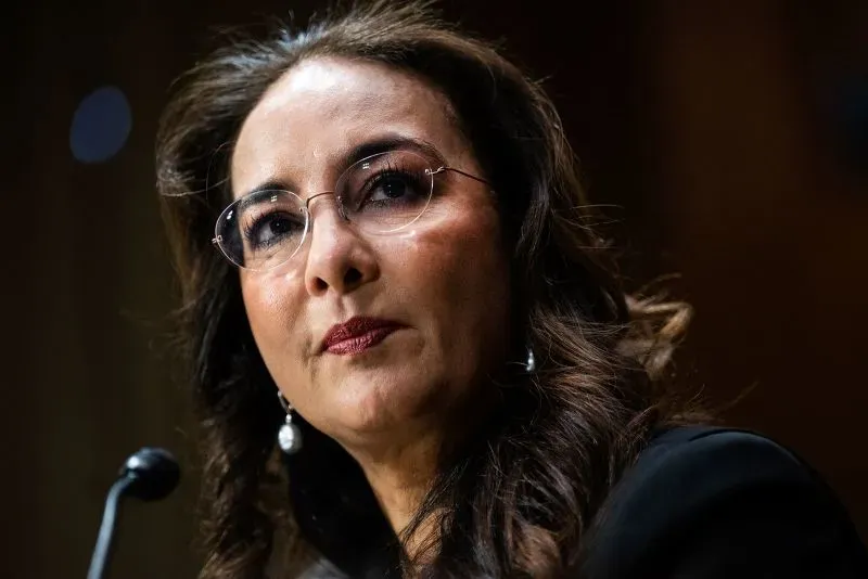 وجه امرأة ترتدي نظارات، تعبر عن الجدية والاهتمام، أثناء حديثها أمام ميكروفون في جلسة رسمية.